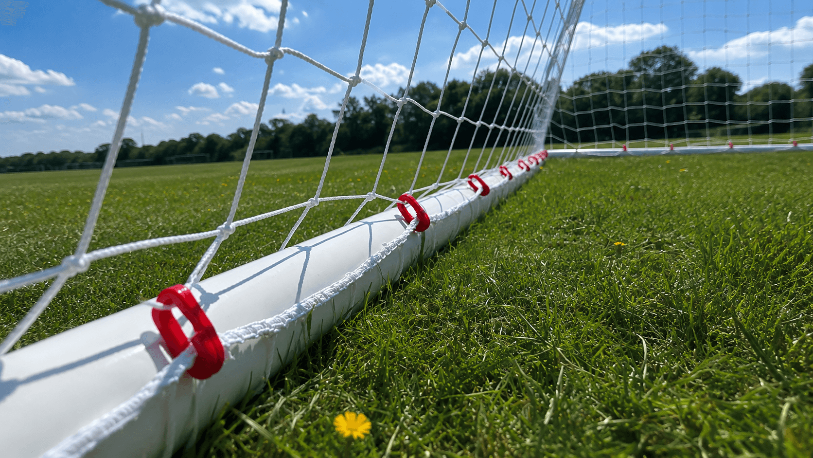 Pitch-level view of a MultiGoal frame with bungee net clips on grass.